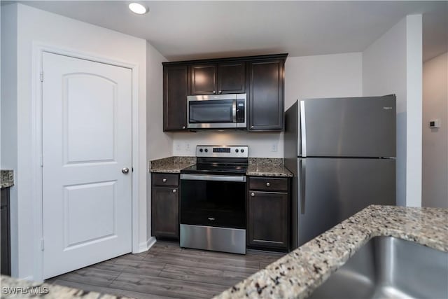 kitchen with dark brown cabinetry, light stone counters, stainless steel appliances, and dark hardwood / wood-style floors