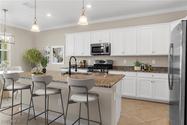 kitchen with a center island with sink, dark stone countertops, pendant lighting, stainless steel appliances, and white cabinets