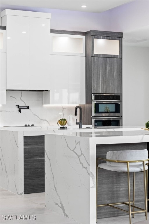 kitchen featuring tasteful backsplash, white cabinets, light stone counters, and double oven