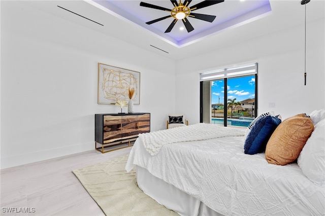 bedroom featuring access to outside, a tray ceiling, hardwood / wood-style floors, and ceiling fan