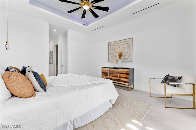 bedroom featuring ceiling fan, a tray ceiling, and wood-type flooring