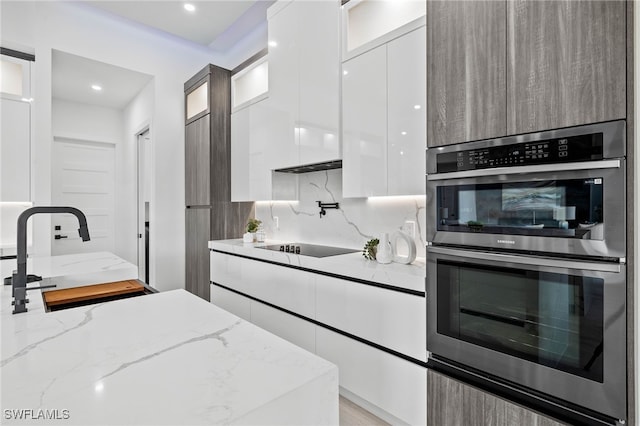 kitchen with black electric cooktop, light stone counters, white cabinets, double oven, and sink