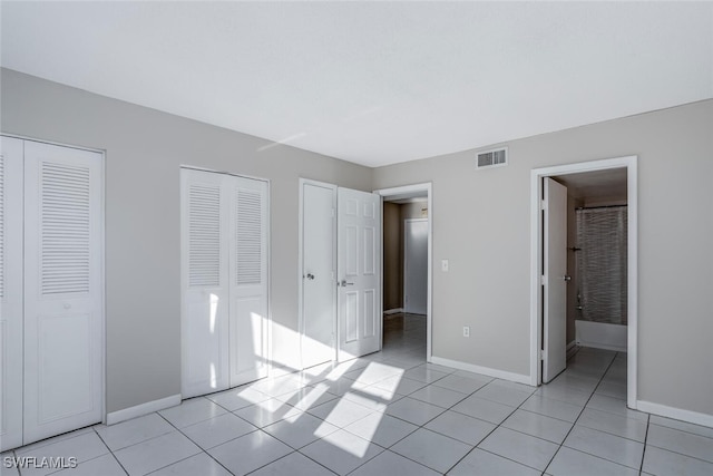 unfurnished bedroom featuring multiple closets, ensuite bathroom, and light tile patterned floors