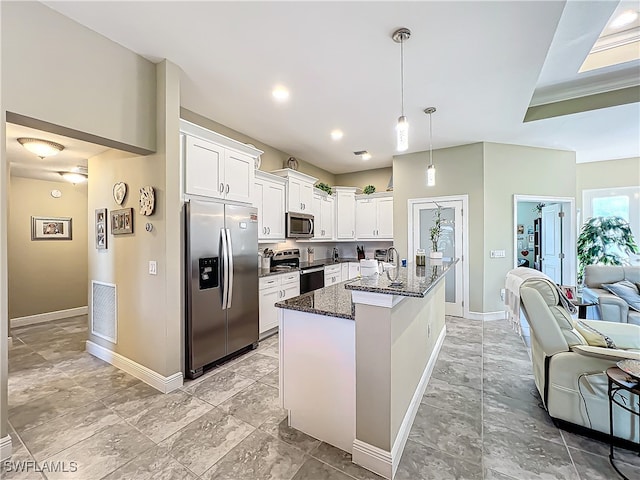 kitchen with white cabinetry, dark stone countertops, decorative light fixtures, a center island with sink, and appliances with stainless steel finishes