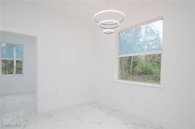 spare room featuring marble finish floor, plenty of natural light, and baseboards