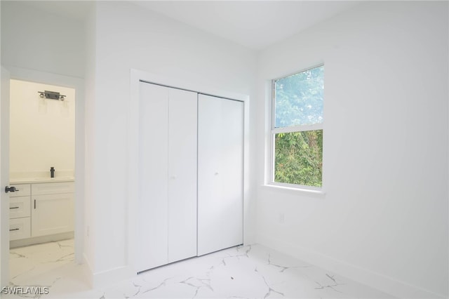 unfurnished bedroom featuring marble finish floor, a closet, ensuite bath, and baseboards