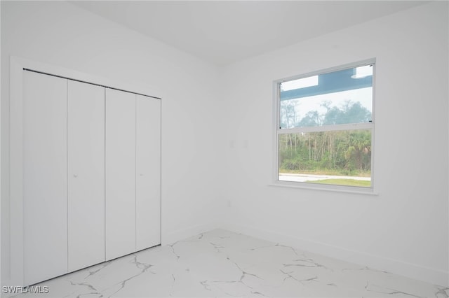 unfurnished bedroom with marble finish floor, a closet, and baseboards