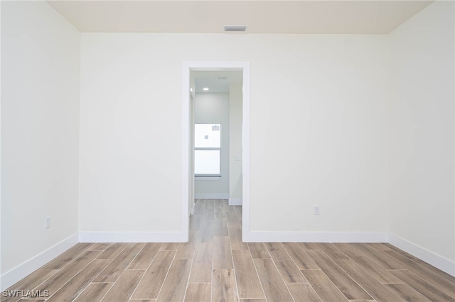 spare room with light wood-type flooring, visible vents, and baseboards