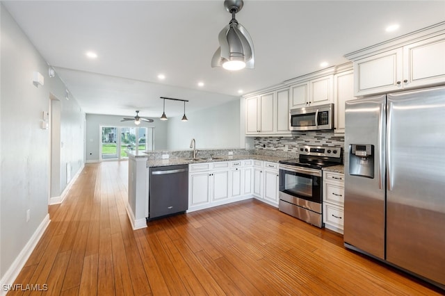 kitchen with decorative backsplash, appliances with stainless steel finishes, a sink, light wood-type flooring, and a peninsula