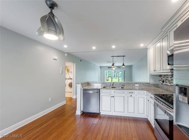 kitchen featuring dark wood-style floors, tasteful backsplash, appliances with stainless steel finishes, a sink, and a peninsula