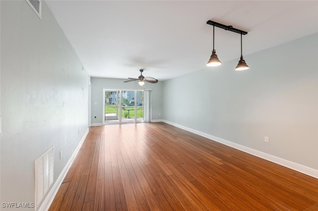 empty room with hardwood / wood-style flooring, baseboards, visible vents, and a ceiling fan