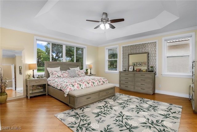 bedroom with ornamental molding, light wood-type flooring, ceiling fan, and a raised ceiling