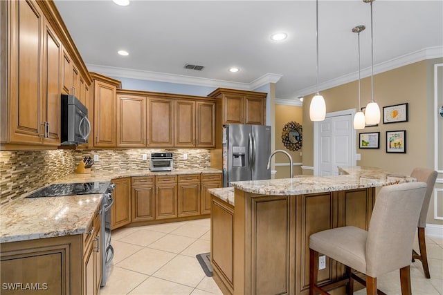 kitchen featuring a kitchen island with sink, ornamental molding, hanging light fixtures, appliances with stainless steel finishes, and light tile patterned floors