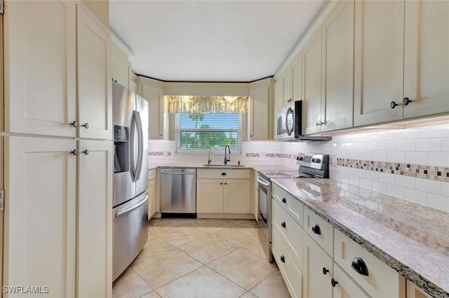 kitchen with sink, stainless steel appliances, backsplash, light stone countertops, and cream cabinets