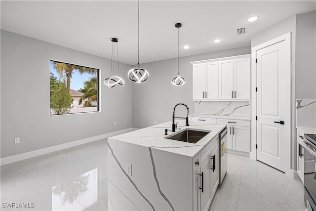 kitchen featuring a kitchen island with sink, sink, decorative light fixtures, white cabinets, and light stone counters