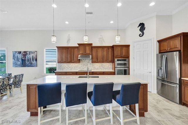 kitchen with a kitchen island with sink, hanging light fixtures, stainless steel appliances, ornamental molding, and a kitchen bar