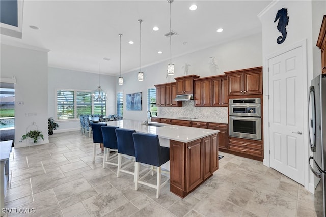 kitchen with tasteful backsplash, a center island with sink, appliances with stainless steel finishes, a kitchen bar, and decorative light fixtures