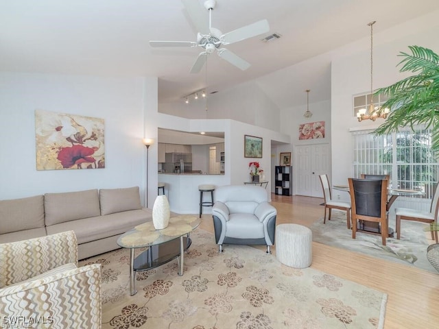 living room featuring ceiling fan with notable chandelier, light hardwood / wood-style floors, and high vaulted ceiling