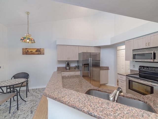 kitchen with hanging light fixtures, light stone countertops, stainless steel appliances, light wood-type flooring, and sink