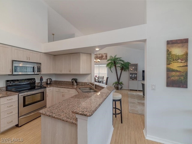 kitchen with sink, kitchen peninsula, a kitchen bar, stainless steel appliances, and light hardwood / wood-style floors