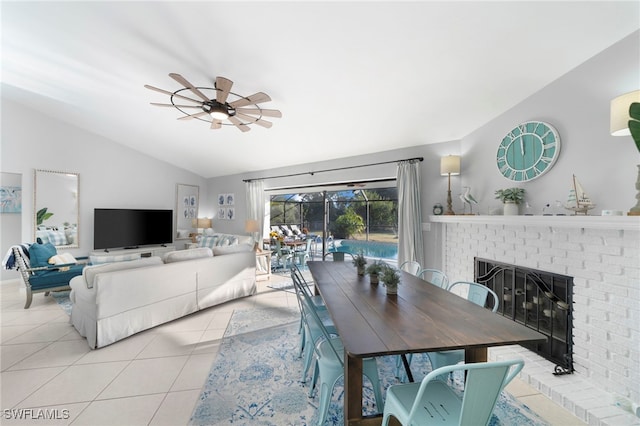 dining area with a ceiling fan, vaulted ceiling, light tile patterned floors, and a fireplace