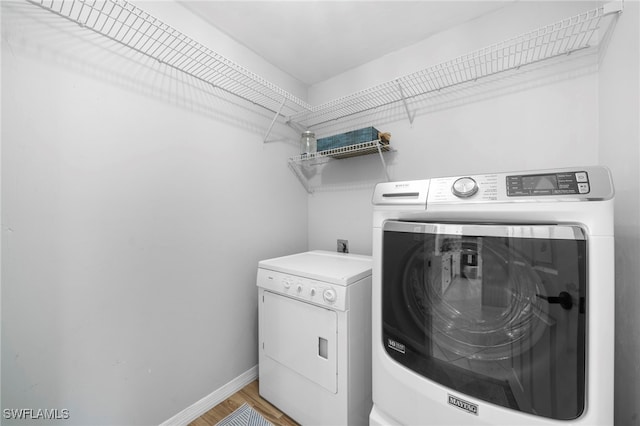 clothes washing area with laundry area, washing machine and dryer, baseboards, and light wood-type flooring