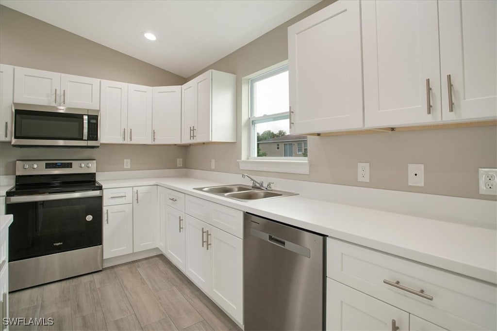 kitchen with stainless steel appliances, lofted ceiling, white cabinets, and sink