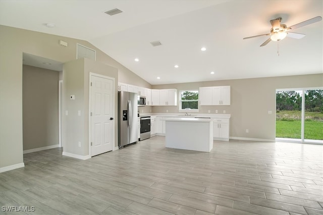 kitchen featuring white cabinets, appliances with stainless steel finishes, a center island, light wood-type flooring, and vaulted ceiling