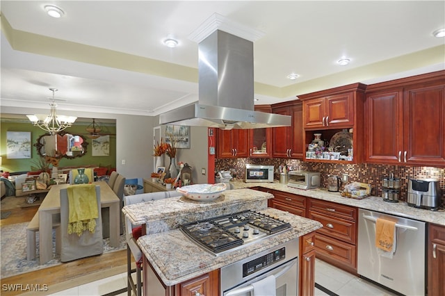 kitchen featuring island exhaust hood, tasteful backsplash, appliances with stainless steel finishes, a chandelier, and a kitchen bar