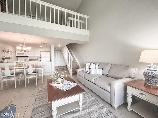 living room with visible vents, a towering ceiling, an inviting chandelier, light tile patterned flooring, and stairs