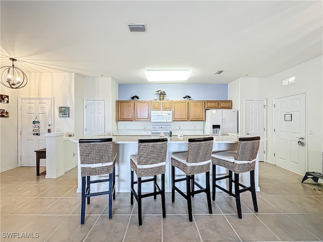 kitchen with hanging light fixtures, a large island, a kitchen bar, light tile patterned floors, and white appliances