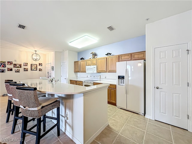 kitchen with white appliances, a breakfast bar area, light tile patterned floors, a chandelier, and a kitchen island with sink