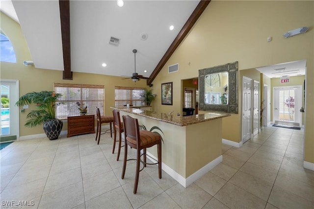 kitchen with high vaulted ceiling, ceiling fan, a breakfast bar area, stone countertops, and light tile patterned floors