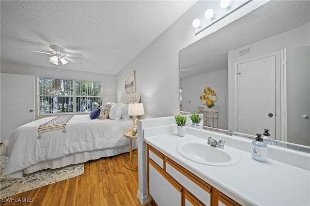 bedroom featuring ceiling fan, sink, light wood-type flooring, and a textured ceiling