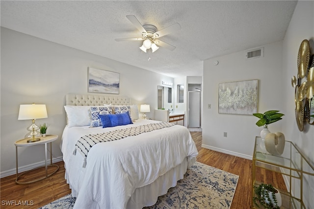 bedroom with ceiling fan, a textured ceiling, ensuite bath, and wood-type flooring