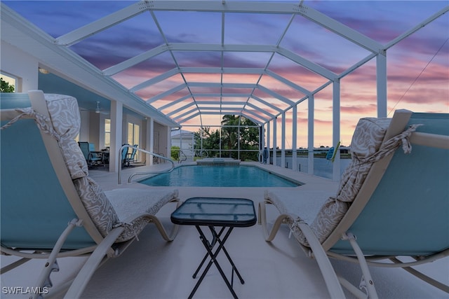 pool at dusk with glass enclosure and a patio area