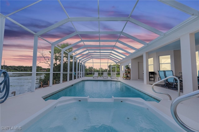 pool at dusk with glass enclosure and a patio area