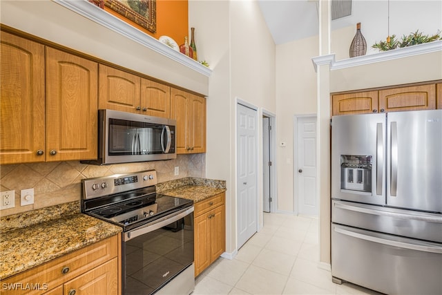 kitchen with decorative backsplash, dark stone counters, a towering ceiling, stainless steel appliances, and light tile patterned floors