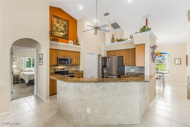 kitchen with dark stone countertops, kitchen peninsula, high vaulted ceiling, appliances with stainless steel finishes, and light tile patterned floors