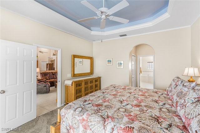 carpeted bedroom with a raised ceiling, ornamental molding, ensuite bathroom, and ceiling fan