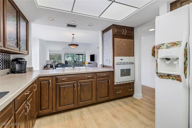 kitchen with kitchen peninsula, white appliances, dark brown cabinets, hanging light fixtures, and light hardwood / wood-style flooring