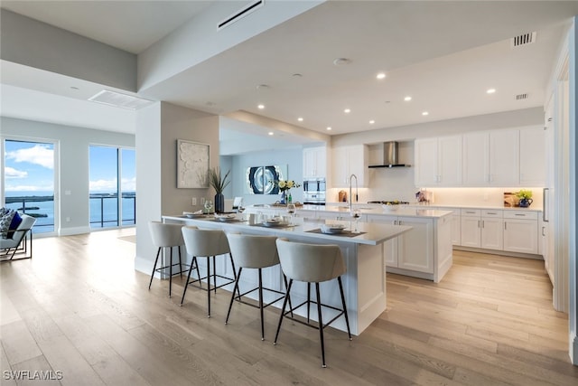 kitchen featuring light hardwood / wood-style floors, a water view, white cabinetry, wall chimney exhaust hood, and a breakfast bar area