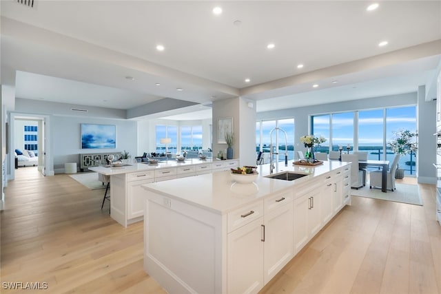 kitchen with white cabinetry, a breakfast bar area, light wood-type flooring, sink, and a spacious island