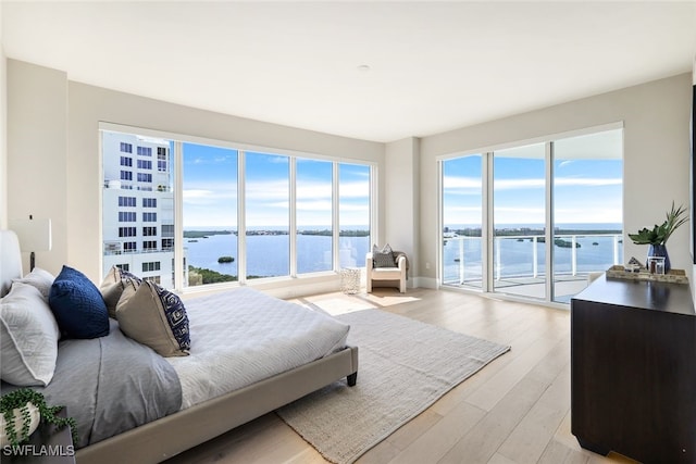 bedroom with light wood-type flooring, a water view, and access to outside