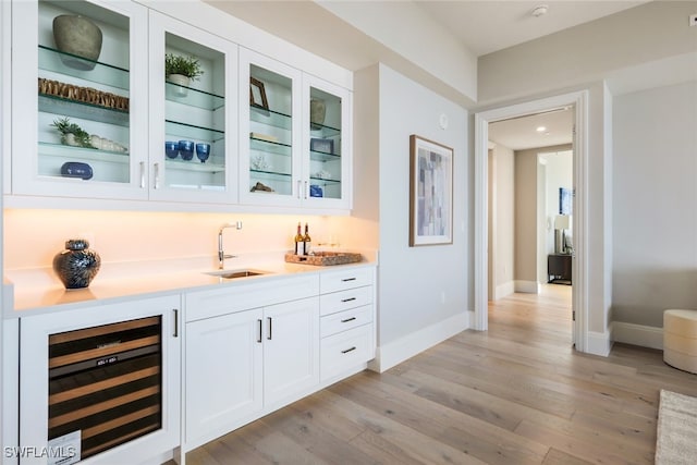 bar with light wood-type flooring, white cabinetry, sink, and wine cooler