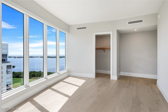 unfurnished bedroom with light wood-type flooring, a closet, a water view, and a spacious closet