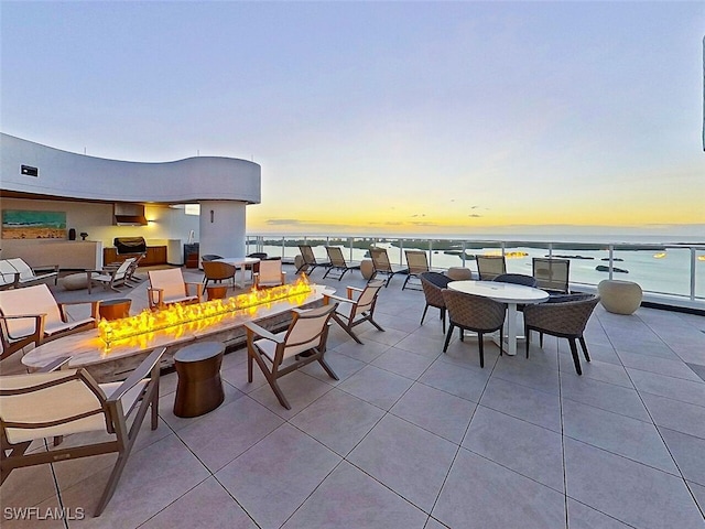 patio terrace at dusk featuring an outdoor living space with a fire pit and a water view