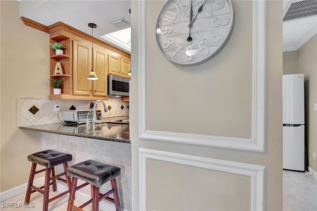 kitchen featuring a kitchen breakfast bar, tasteful backsplash, dark stone counters, white fridge, and hanging light fixtures