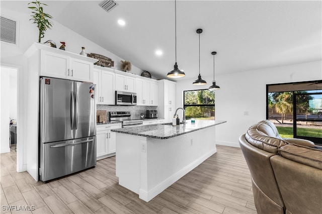 kitchen featuring an island with sink, decorative light fixtures, white cabinetry, stainless steel appliances, and dark stone counters