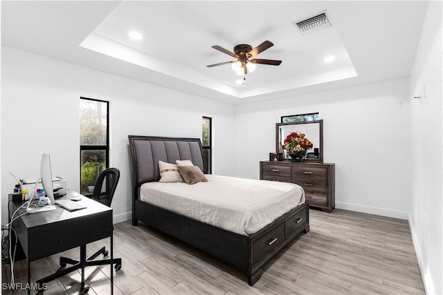 bedroom with multiple windows, a tray ceiling, light wood-type flooring, and ceiling fan